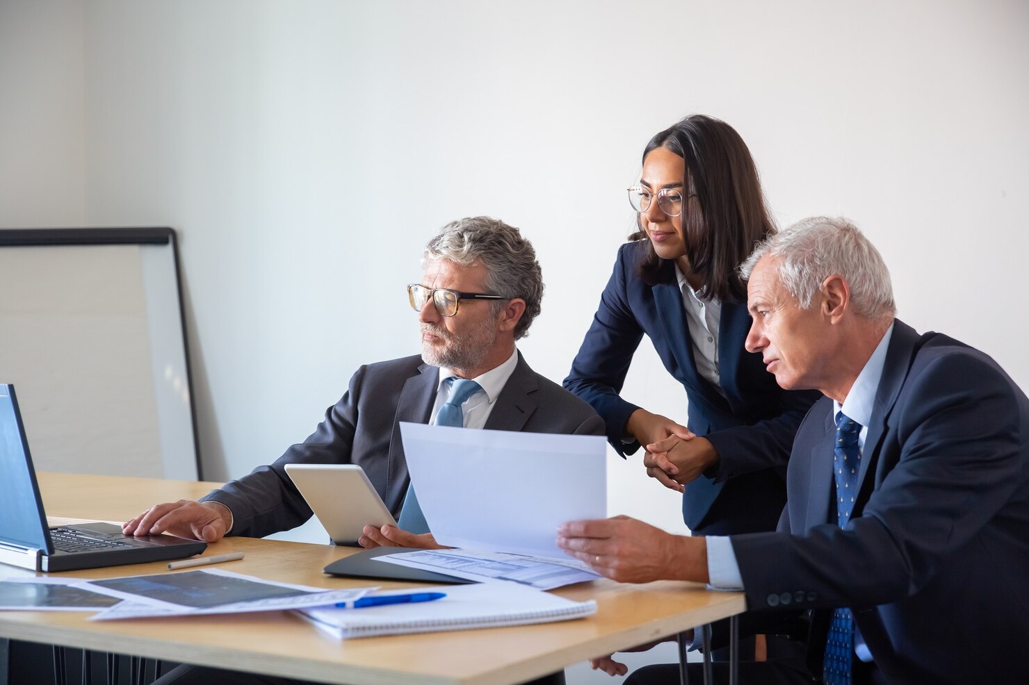 socios concentrados que usan laptop trabajan documentos empresarios serios confiados trajes oficina discutiendo juntos proyecto empresa concepto gestion negocios asociacion